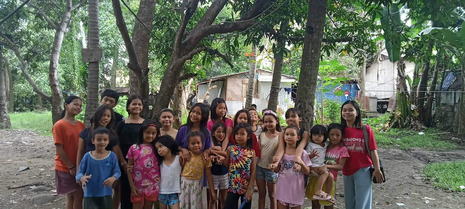 A large group of children gathered under the trees during a Marilog outreach